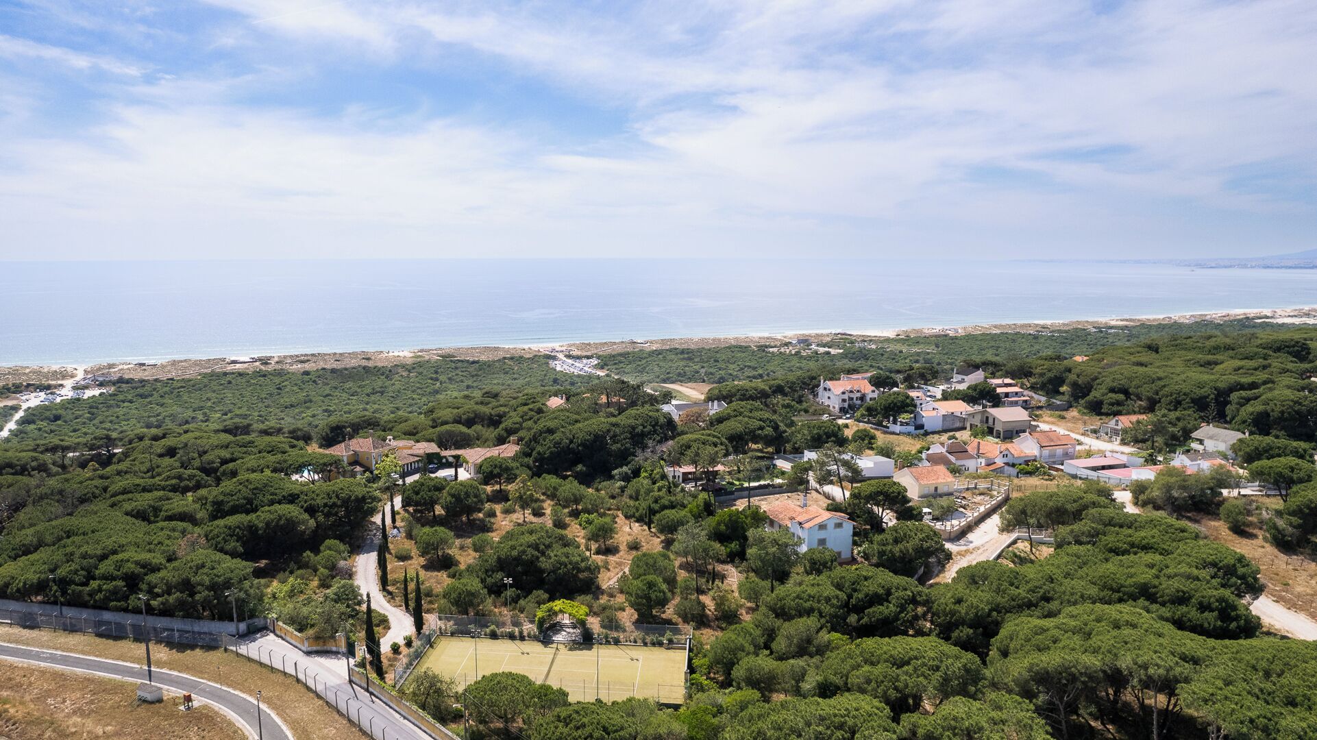 Uma área residencial costeira com casas rodeadas por vegetação densa e vista clara para o mar.