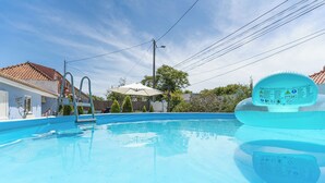 Une piscine avec un escalier, une chaise longue et un espace abrité avec un parasol.