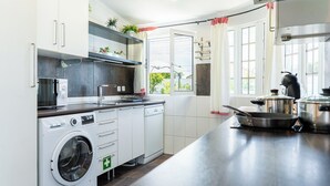 Une cuisine moderne dotée d’un lave-linge et d’un sèche-linge intégrés, d’appareils électroménagers en acier inoxydable et d’une grande fenêtre laissant entrer la lumière naturelle.