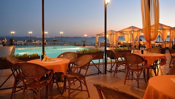 An outdoor dining area with wicker chairs and tables, overlooking a pool and the sea. - Luxury Penthouse Apartment with Panoramic Sea Views (Sveti Vlas)