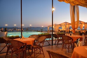 Un área de comedor al aire libre con sillas y mesas de mimbre, con vistas a una piscina y al mar.