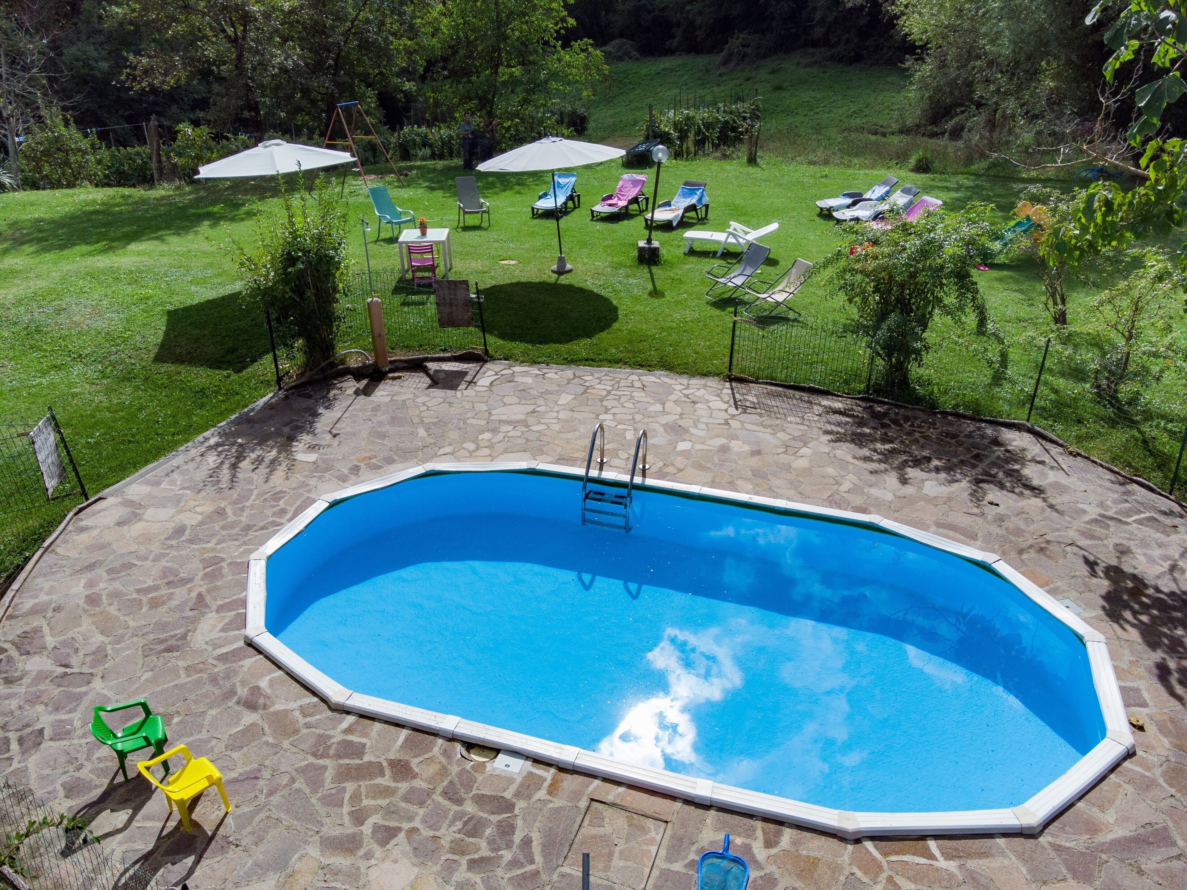 An outdoor swimming pool with a stone deck, surrounded by a grassy area with lounge chairs and umbrellas.