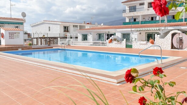 A swimming pool surrounded by white buildings with balconies, a clear sky, and red flowers in the foreground. - Disabled friendly - LUXURY bungalow / Villa , San Eugenio,  Costa Adeje  (Costa Adeje)