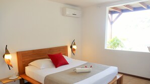 A single bed with a wooden headboard, white bedding, a red pillow, and a small bedside table with a lamp. - ❤F2 luxury, sea view, 2 min from beaches, quiet, nature, wifi, air conditioning (Les Anses-d'Arlet)
