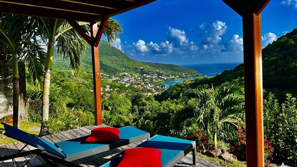 A wooden deck with lounge chairs and red cushions, overlooking a coastal village and mountains. - ❤F2 luxury, sea view, 2 min from beaches, quiet, nature, wifi, air conditioning (Les Anses-d'Arlet)
