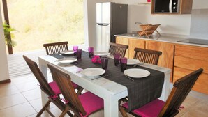A dining area with a table set for four, a refrigerator, and a microwave in the kitchen area. - ❤F2 luxury, sea view, 2 min from beaches, quiet, nature, wifi, air conditioning (Les Anses-d'Arlet)