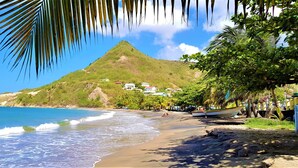 A beach with a mountain in the background, clear blue water, and some buildings on the hillside. - ❤F2 luxury, sea view, 2 min from beaches, quiet, nature, wifi, air conditioning (Les Anses-d'Arlet)