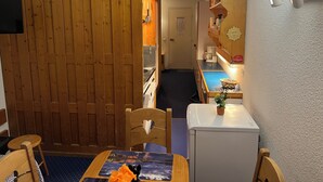 A cozy room with a wooden door, a small kitchenette, a dining area with a table and chairs, and a refrigerator. - Les Arcs 1800: studio - 1 room - 4/5 persons (Bourg-Saint-Maurice)