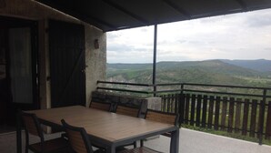 An outdoor patio with a table and chairs, a stone wall, and a view of green hills. - House / Villa - SampzonHouse with garden (Sampzon)