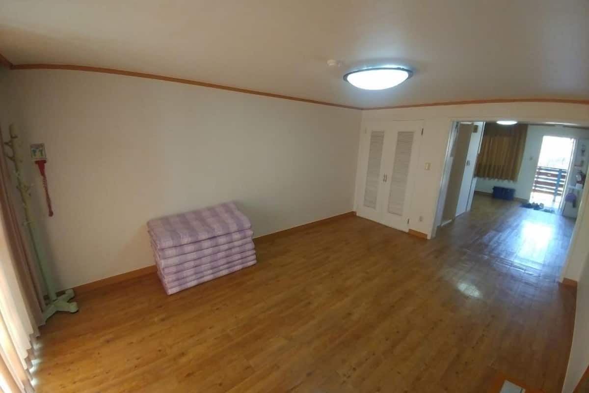 Una habitación amplia con piso de madera, una lámpara en el techo, un armario con puertas y un pasillo que conduce a otra habitación.