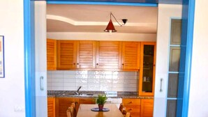 A kitchen with wooden cabinets, a tiled backsplash, and a dining table with chairs. - Casa Palme, APARTMENT AT SEA (Marzamemi)