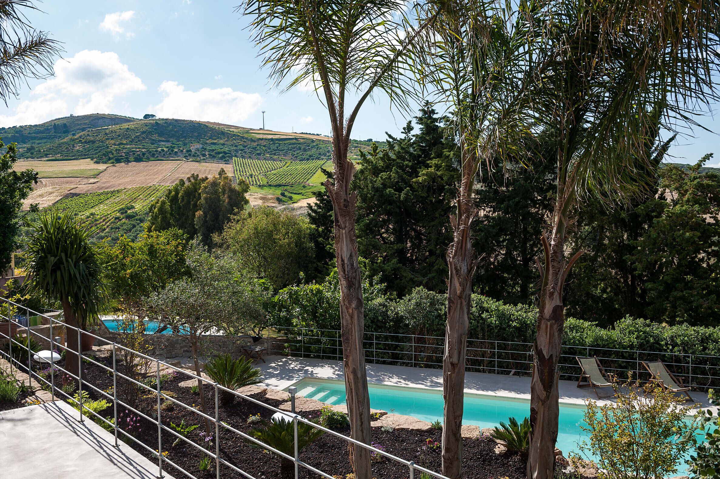 A pool area with lounge chairs, surrounded by trees and a view of vineyards.