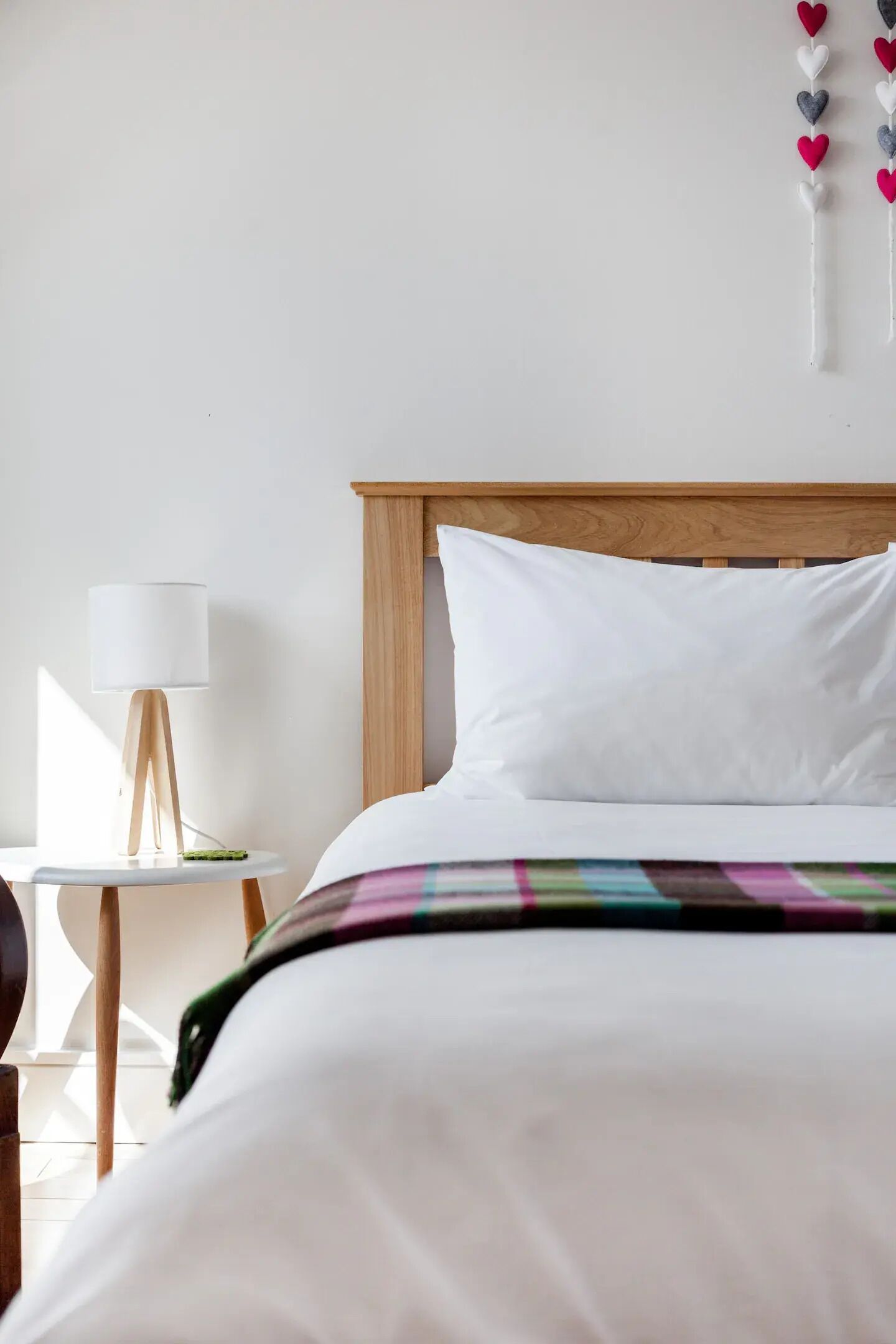 A neatly made bed with white bedding, a wooden headboard, and a small bedside table with a lamp.