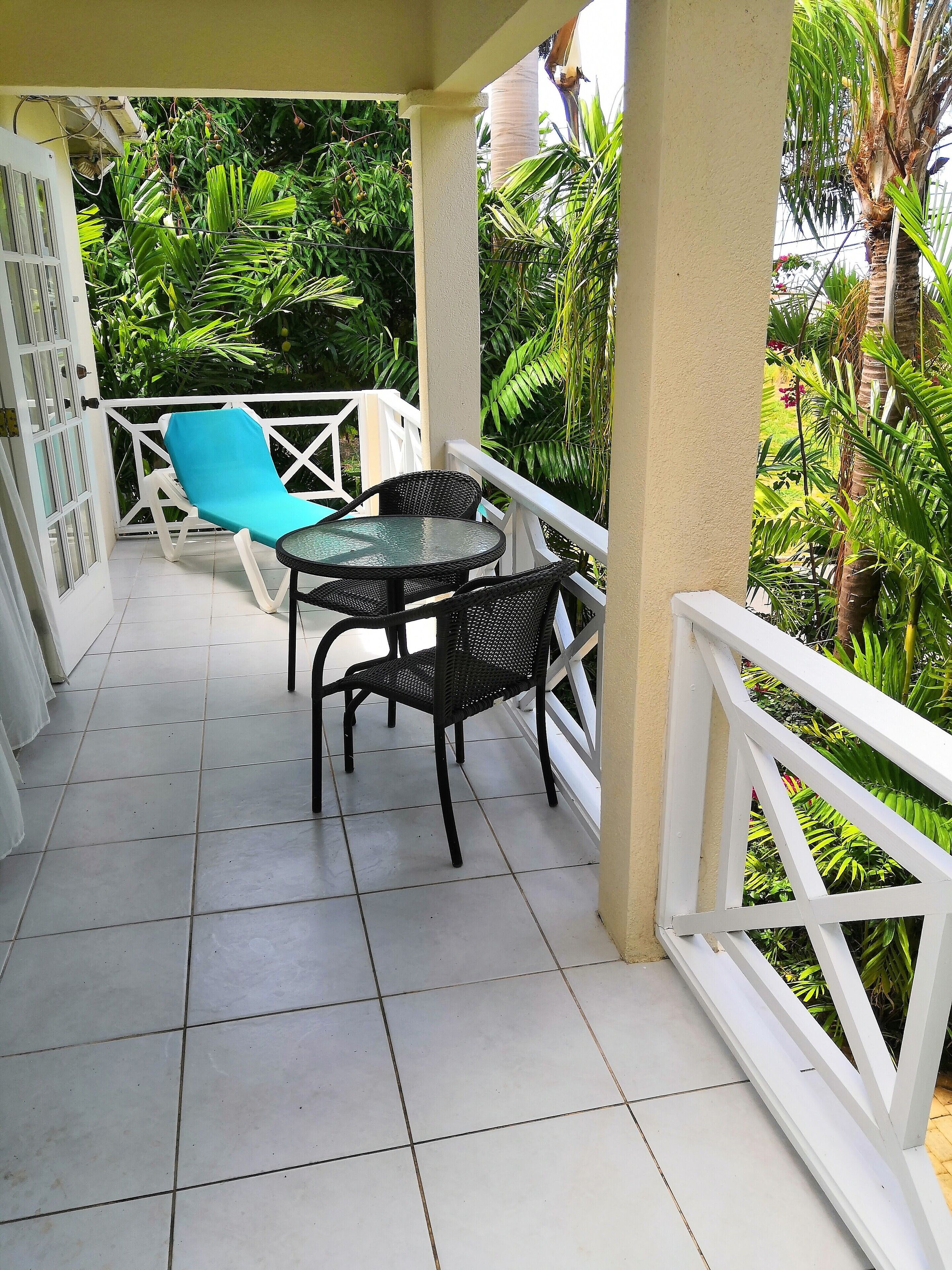 A covered outdoor area with a tiled floor, a white railing, and a table with chairs.