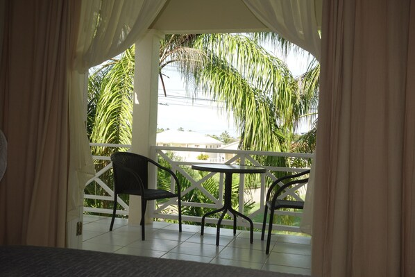A balcony with a table and chairs, overlooking a garden with palm trees.