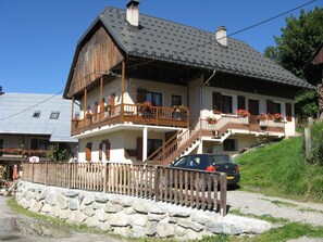 A two-story building with balconies, a stone wall in front, and a car parked nearby. - Chimney sweep in the hamlet of La Chal (Saint-Jean-D'arves)