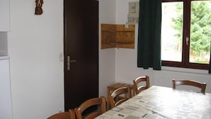 A dining area with a table set for four, wooden chairs, a dark wooden door, and a window with a view of greenery outside. - Chimney sweep in the hamlet of La Chal (Saint-Jean-D'arves)