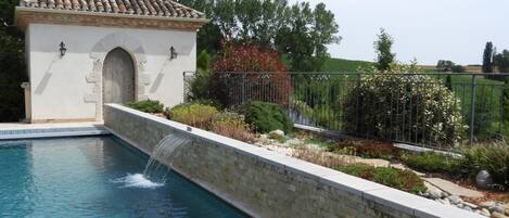 A swimming pool with a stone wall and a small building with an arched entrance.