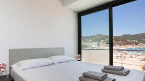 Habitación de hotel con cama, mesita de noche y un amplio ventanal con vista a la playa.
