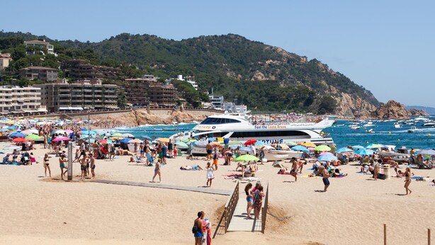 Una playa concurrida con gente, sombrillas y barcos.