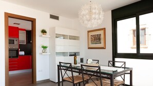 Una cocina moderna con armarios rojos, una zona de comedor con mesa de vidrio y sillas tejidas, y un ventanal con vistas.