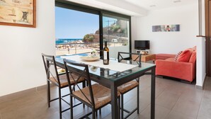 Una sala de estar moderna con una mesa de comedor de vidrio, un sofá rojo y un ventanal con vista a la playa.