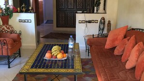 Una sala de estar con suelo estampado, un sofá con cojines, una mesa de centro con frutas y una botella, y una puerta decorativa con diseños intrincados.