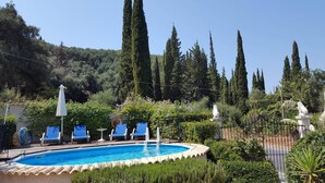 Ein Poolbereich mit blauen Liegestühlen, einem weißen Sonnenschirm und einer Statue im Hintergrund.