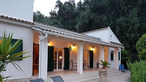 Eine Villa mit überdachter Terrasse, Sitzgelegenheiten im Freien und einem Garten.