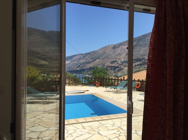 A pool area with a view of mountains, a wooden fence, and a tiled patio.