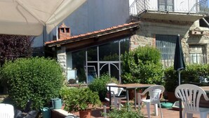 Un patio al aire libre con una mesa y sillas, rodeado de plantas en macetas y un muro de piedra.