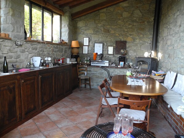 A rustic kitchen with stone walls, wooden cabinets, and a large dining table.