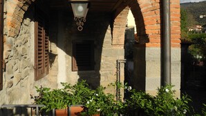 Una entrada de piedra arqueada con un farol colgante, contraventanas de madera y plantas en macetas.