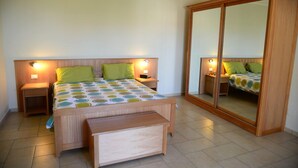 Une chambre à coucher comprenant un lit, des tables de chevet, une commode, un banc en bois et un grand miroir.
