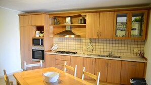 Une cuisine de taille réduite, dotée de meubles en bois, d’une cuisinière, d’un four à micro-ondes et d’un pare-feu en carreaux.