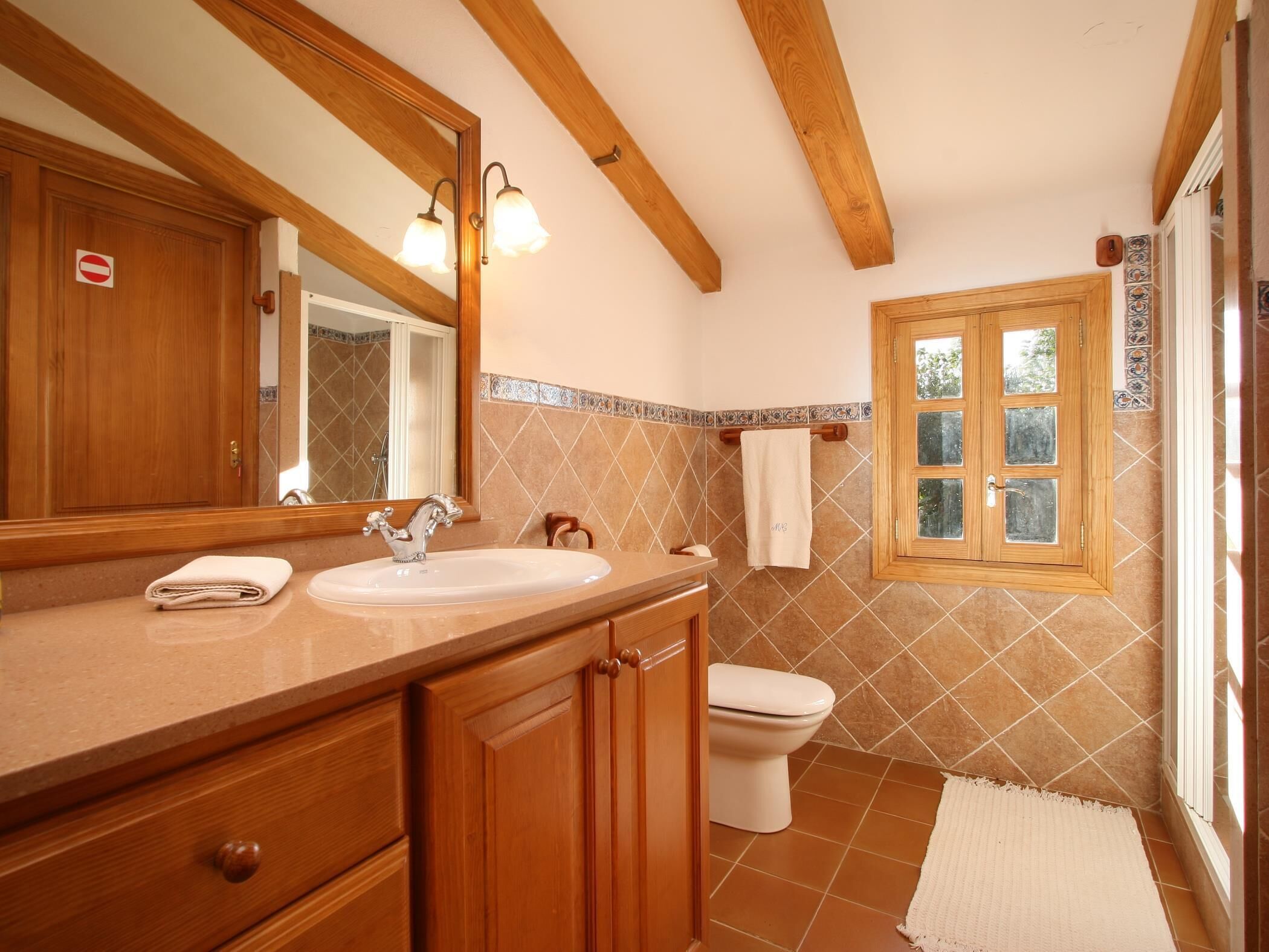 A bathroom with a wooden vanity, a sink, a mirror, a toilet, and a window with a view of greenery.