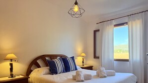 Ein ordentlich gemachtes Bett mit Kissen, einer Nachttischlampe und einem Fenster mit Vorhängen.