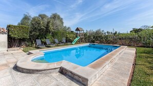 Ein rechteckiger Swimmingpool mit einer grünen Rutsche, umgeben von Steinplatten und einer Rasenfläche.