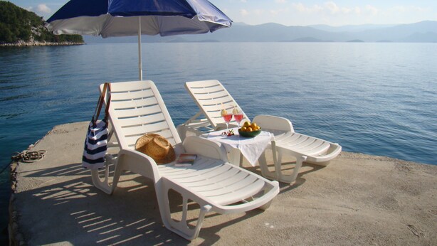 Two white lounge chairs with a table and a blue umbrella on a concrete platform by a body of water. - MAGICAL HOUSE " MARICA" WITH PRIVATE BEACH, PARADISE  FAR AWAY FROM STRESS LIFE (Klek)
