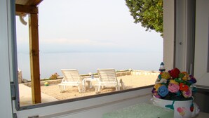 A room with a view of the beach, a window with a wooden frame, a white table with a crocheted flower arrangement, and a decorative box. - MAGICAL HOUSE " MARICA" WITH PRIVATE BEACH, PARADISE  FAR AWAY FROM STRESS LIFE (Klek)