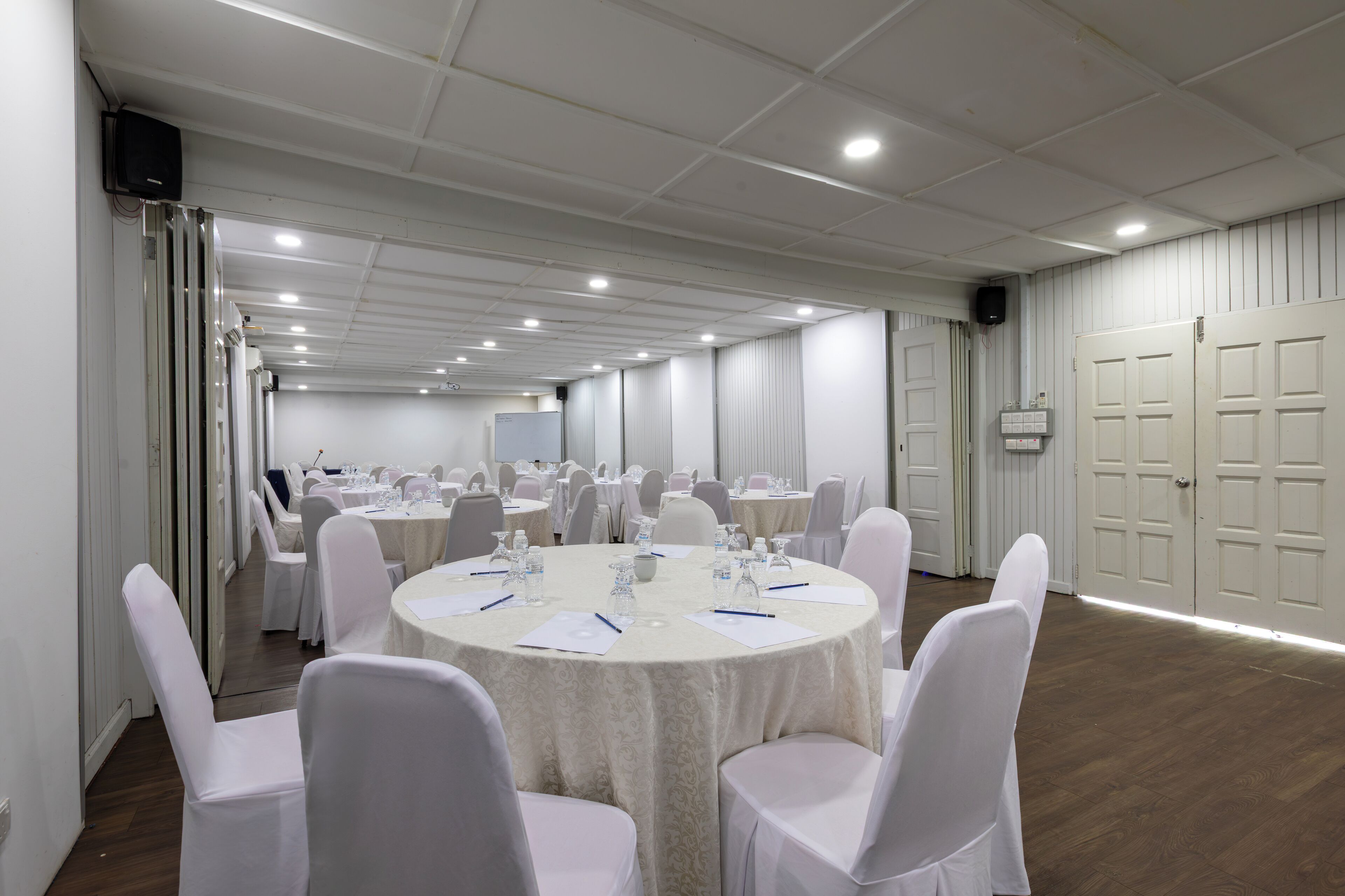 Un salón de conferencias con mesas redondas, sillas blancas y techo blanco.