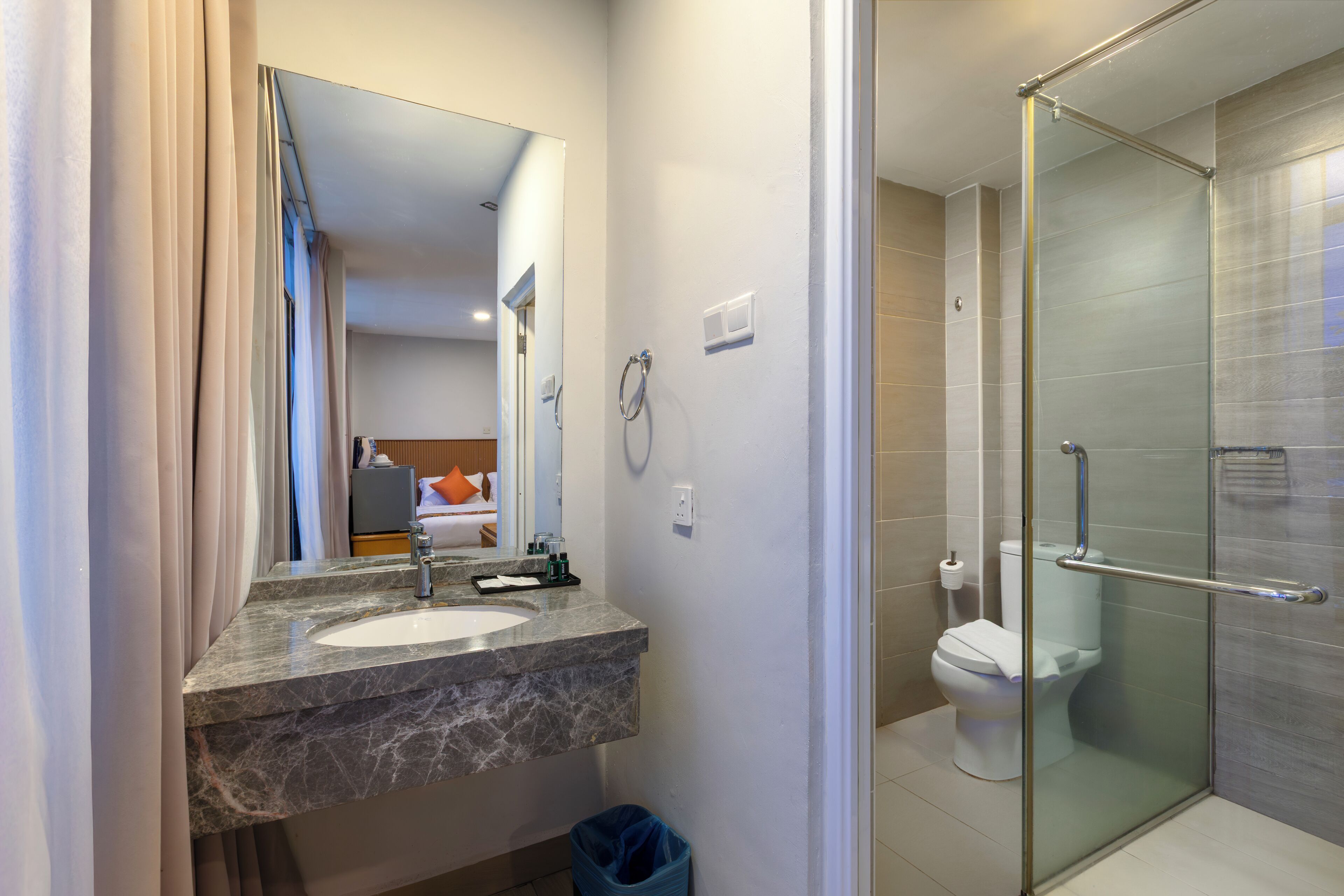Un baño con lavamanos de mármol, cabina de ducha con mampara de vidrio y un inodoro.