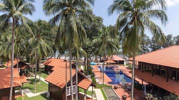 A resort with a swimming pool, palm trees, and red-roofed buildings.