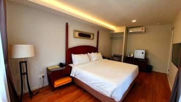 A hotel room with a large bed, a bedside table, a lamp, a flat-screen TV, and a wall-mounted air conditioning unit.