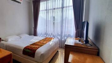 A hotel room with a bed, a desk, a chair, an air conditioner, and a window with curtains.