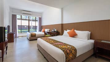 Habitación de hotel con una cama grande, una cama más pequeña, un escritorio, un televisor y una ventana con cortinas.