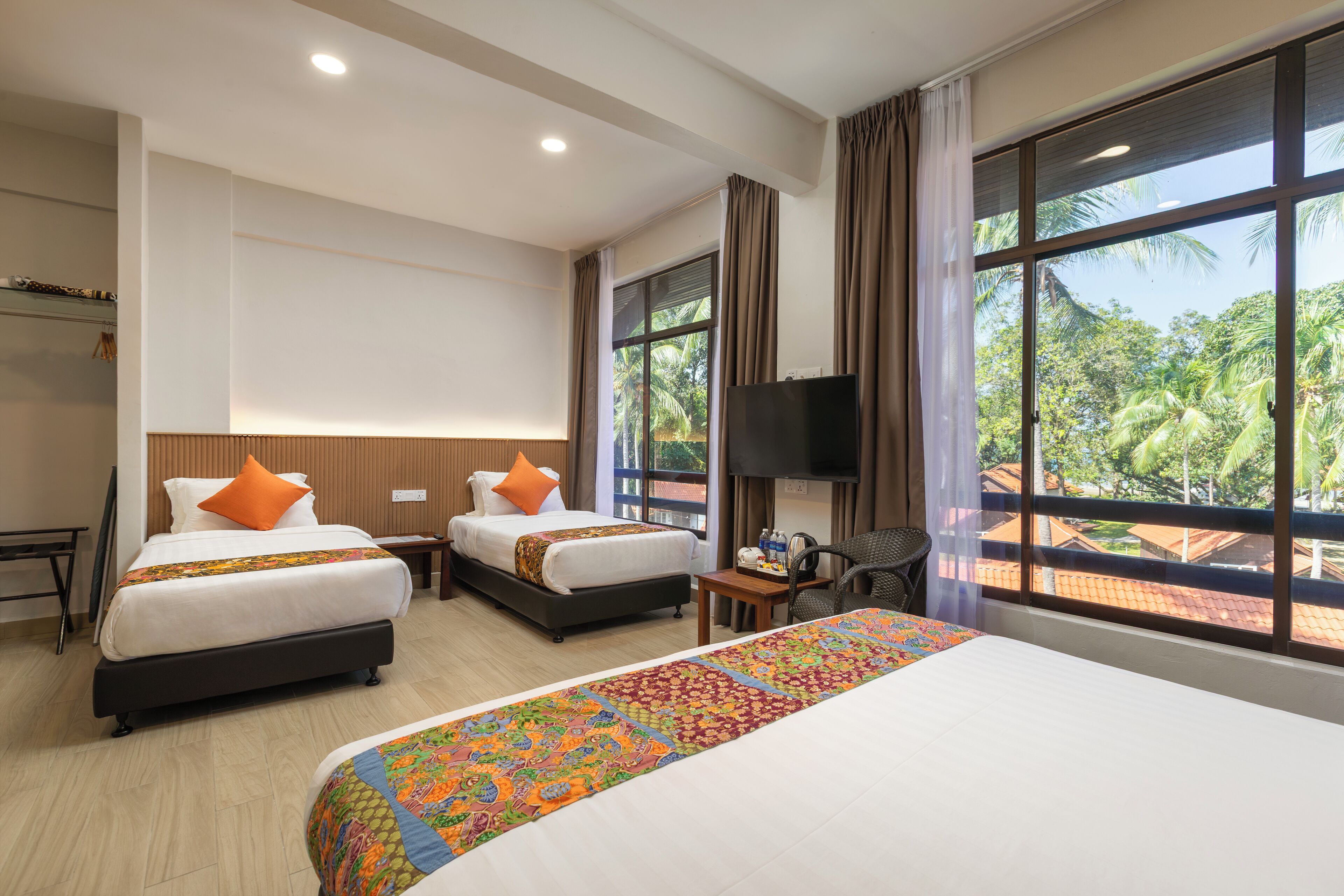 A hotel room with two beds, a TV, a desk, and large windows with a view of palm trees.