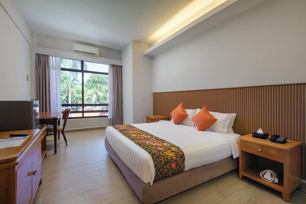 A hotel room with a bed, bedside table, nightstand, desk, chair, and a window with curtains.
