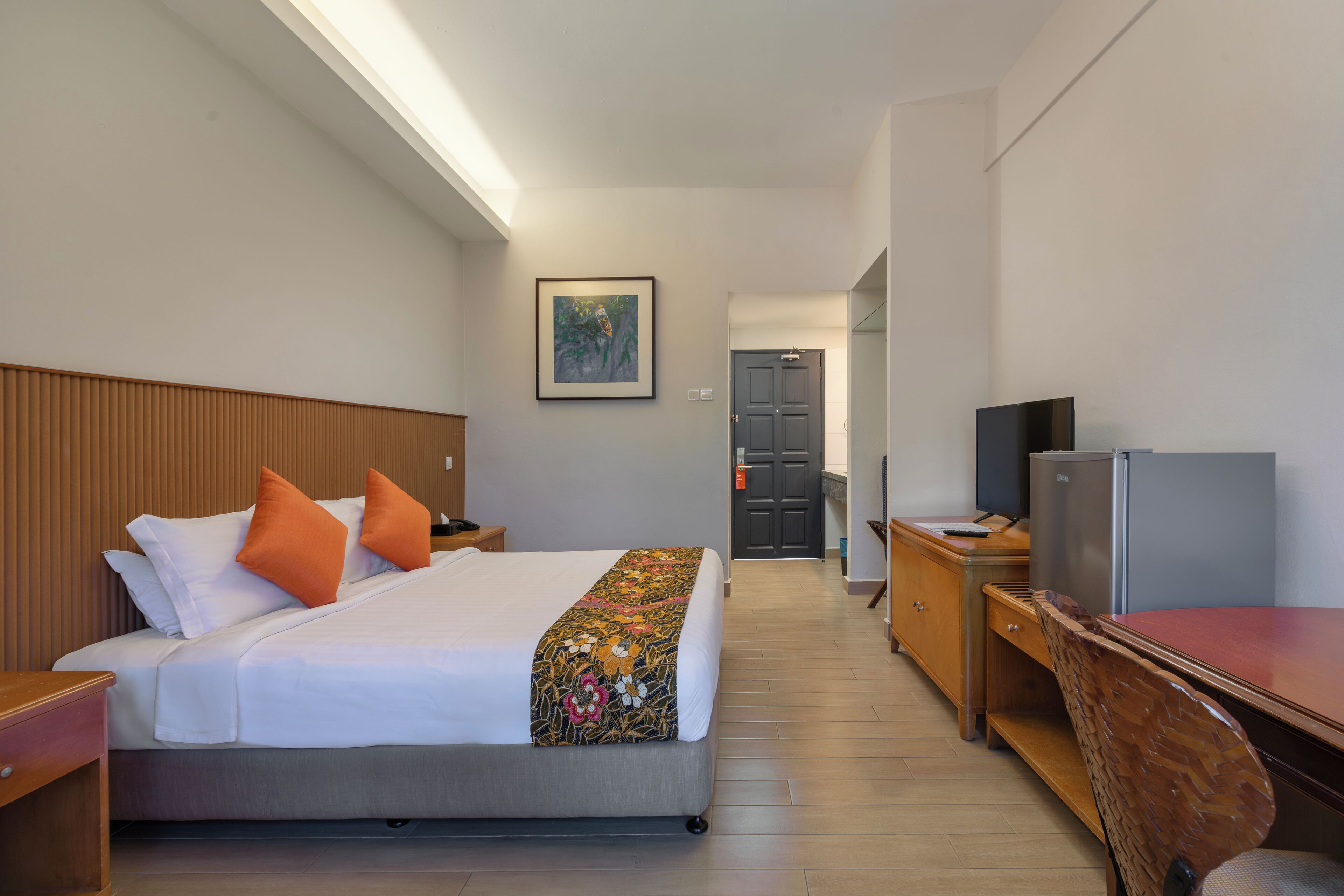 A hotel room with a bed, a desk, a television, and a door leading to another room.