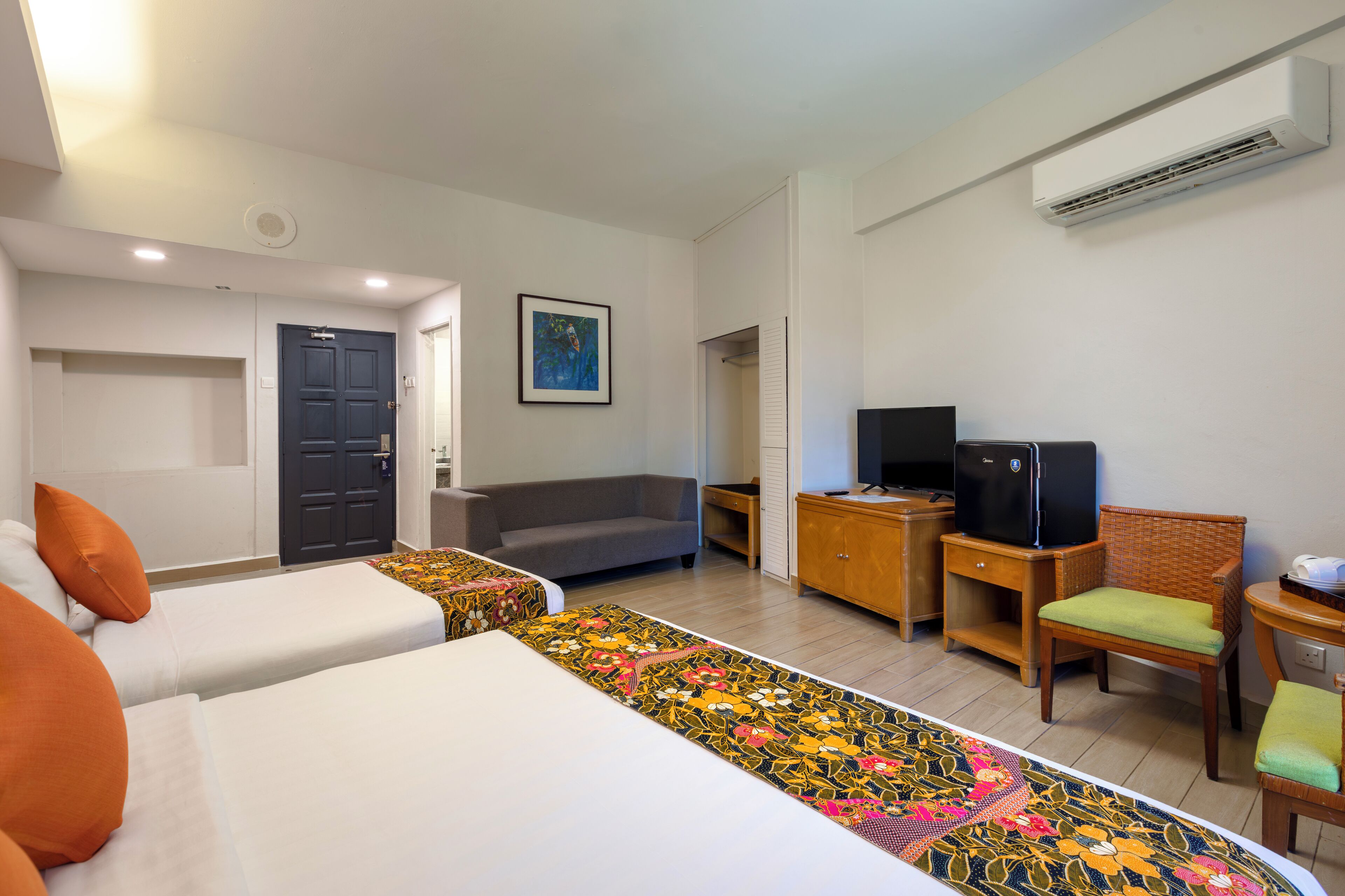 A hotel room with two beds, a sofa, a television, and a desk.